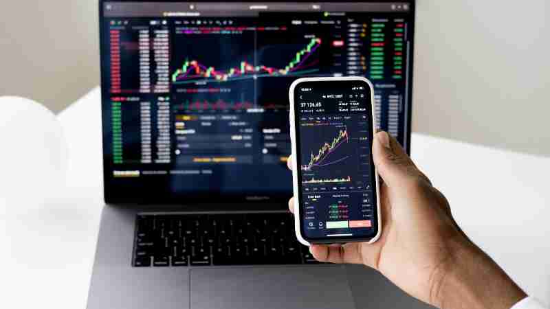 Person checking stock market graphs on laptop and smartphone, focusing on financial data., tags: und - pexel