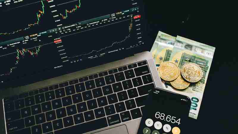 A laptop displaying stock charts with Bitcoin, Euros, and a cellphone calculator, showcasing financial analysis., tags: fokus - pexel